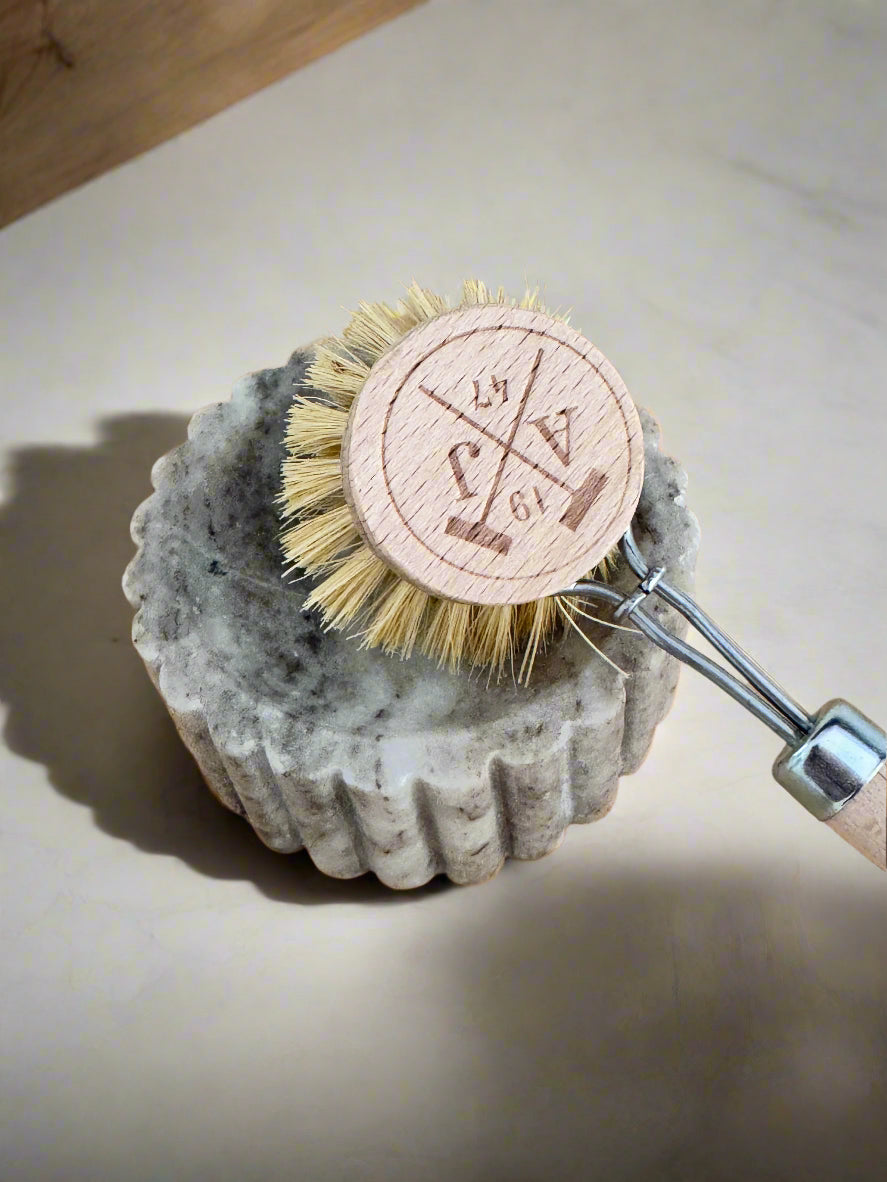 Cleaning brush with a wooden handle and bristles on a stone base against a wooden background