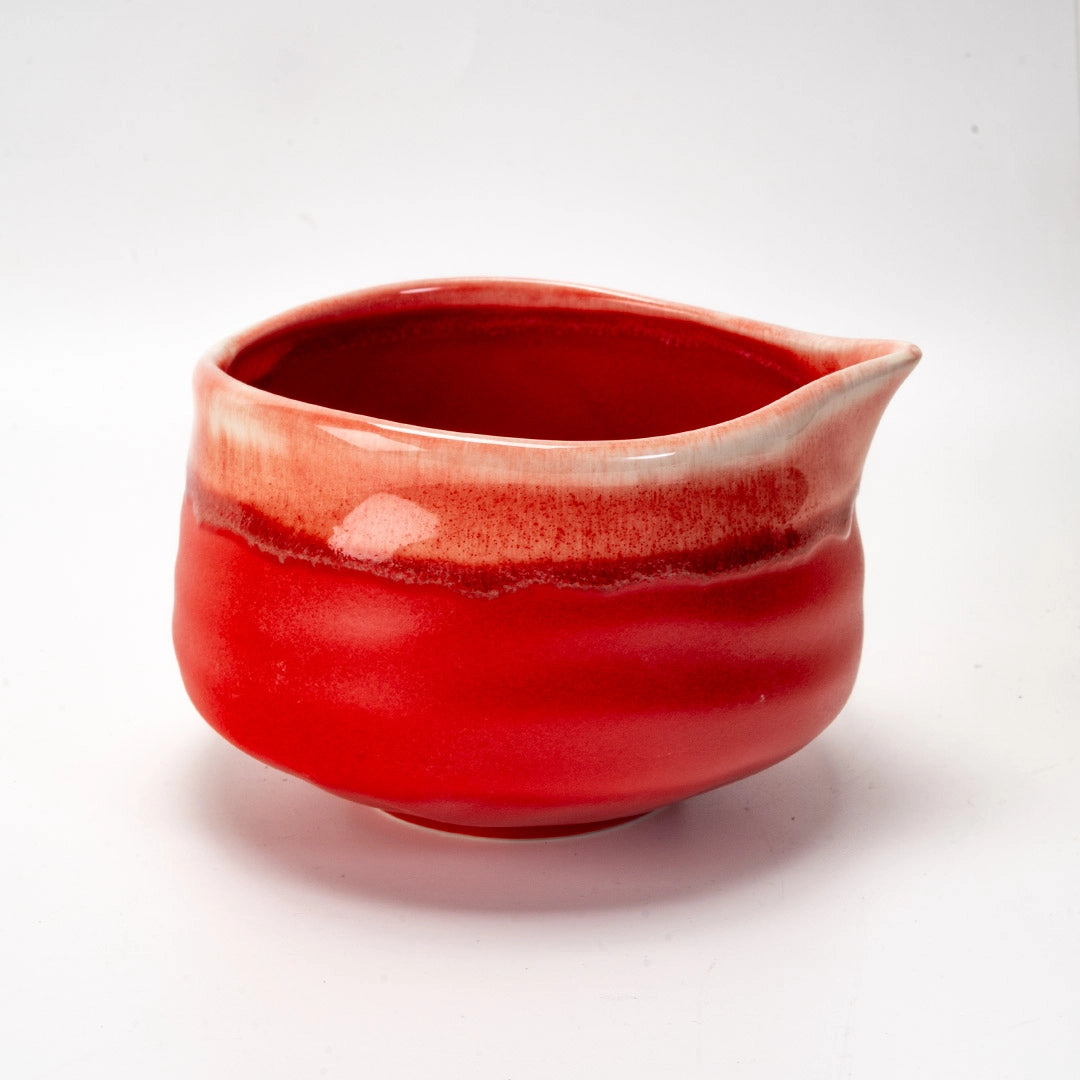 Red ceramic matcha bowl with a white interior on a light gray background